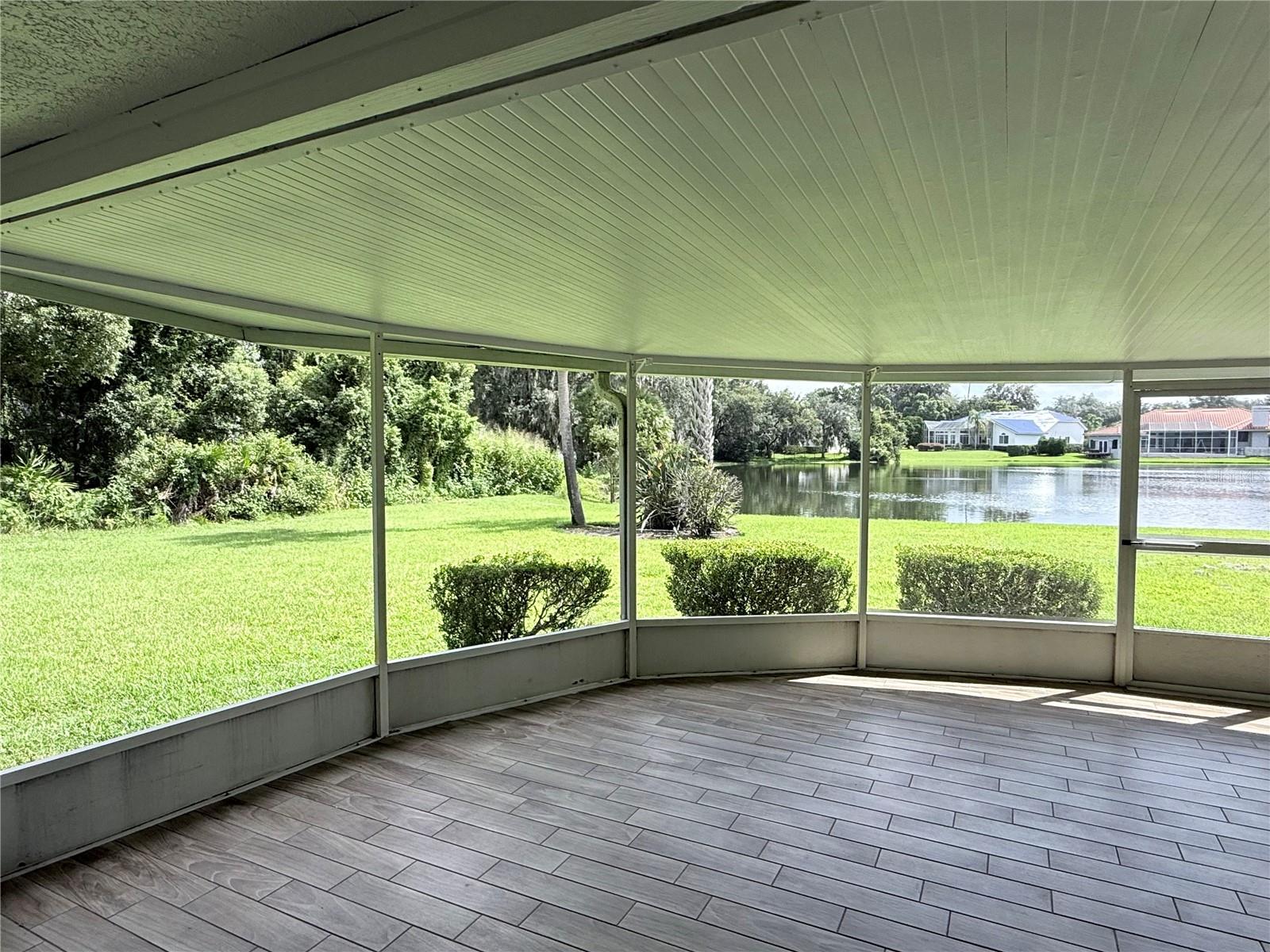 Screened-in patio with gray tile flooring overlooking a lawn and lake.