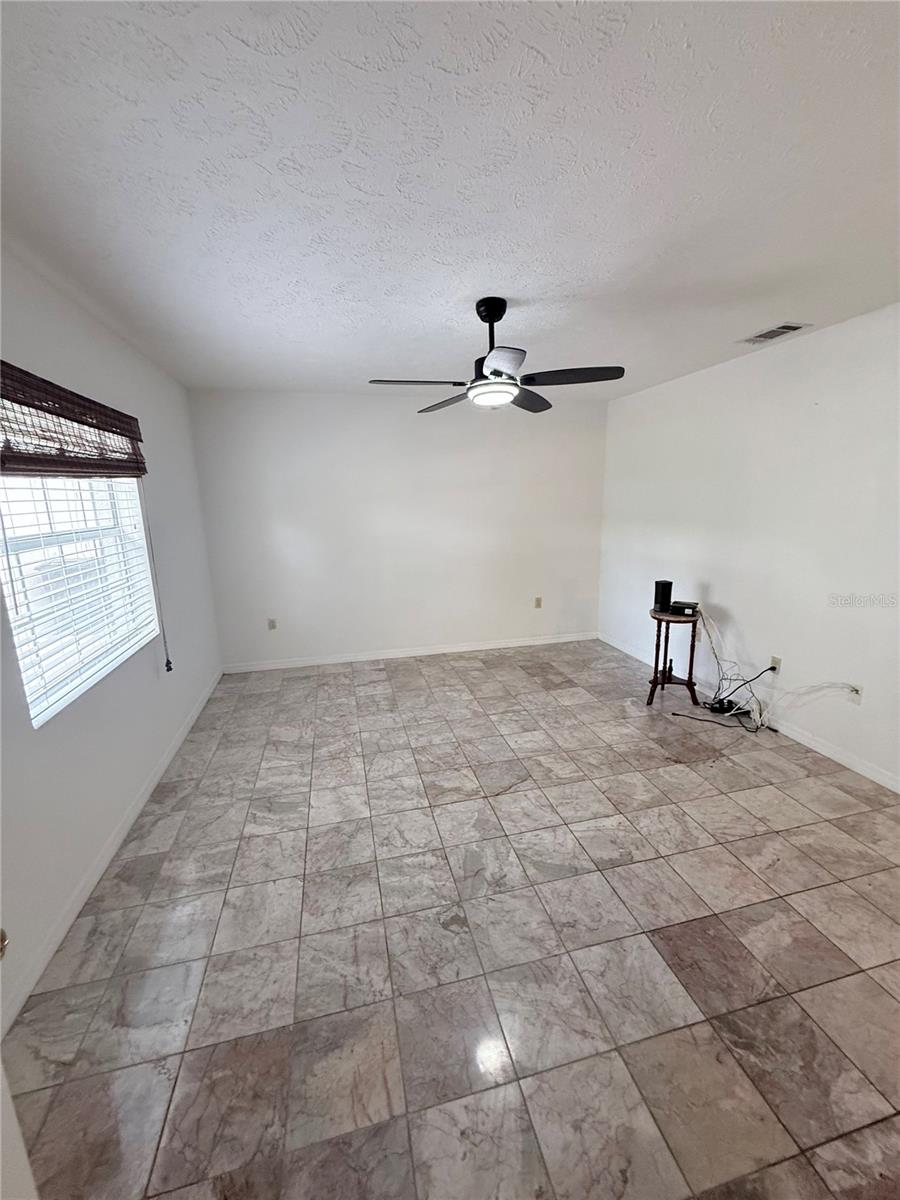 Empty room with marbled tile flooring, a ceiling fan, and a window with blinds.