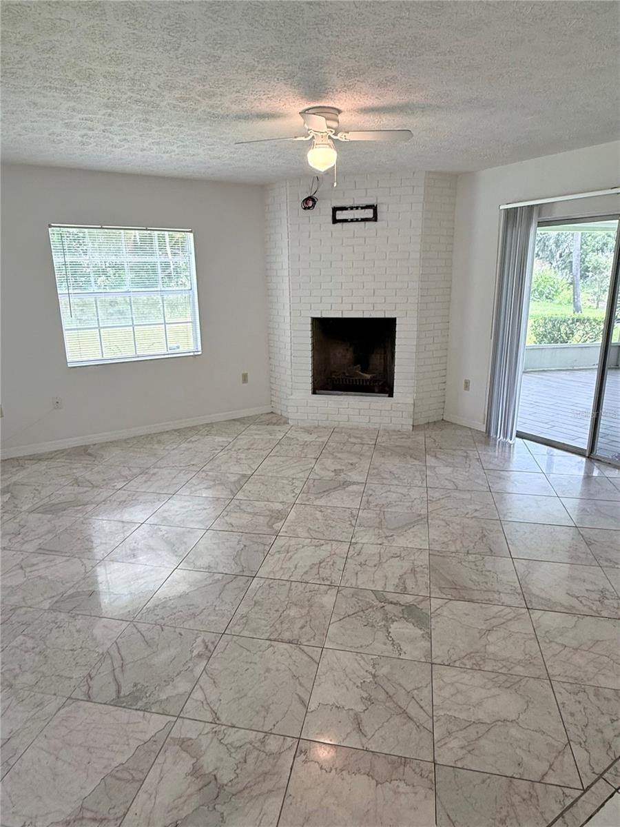 Vacant living room with a white brick fireplace, marble-look tile floor, and sliding doors to a patio.