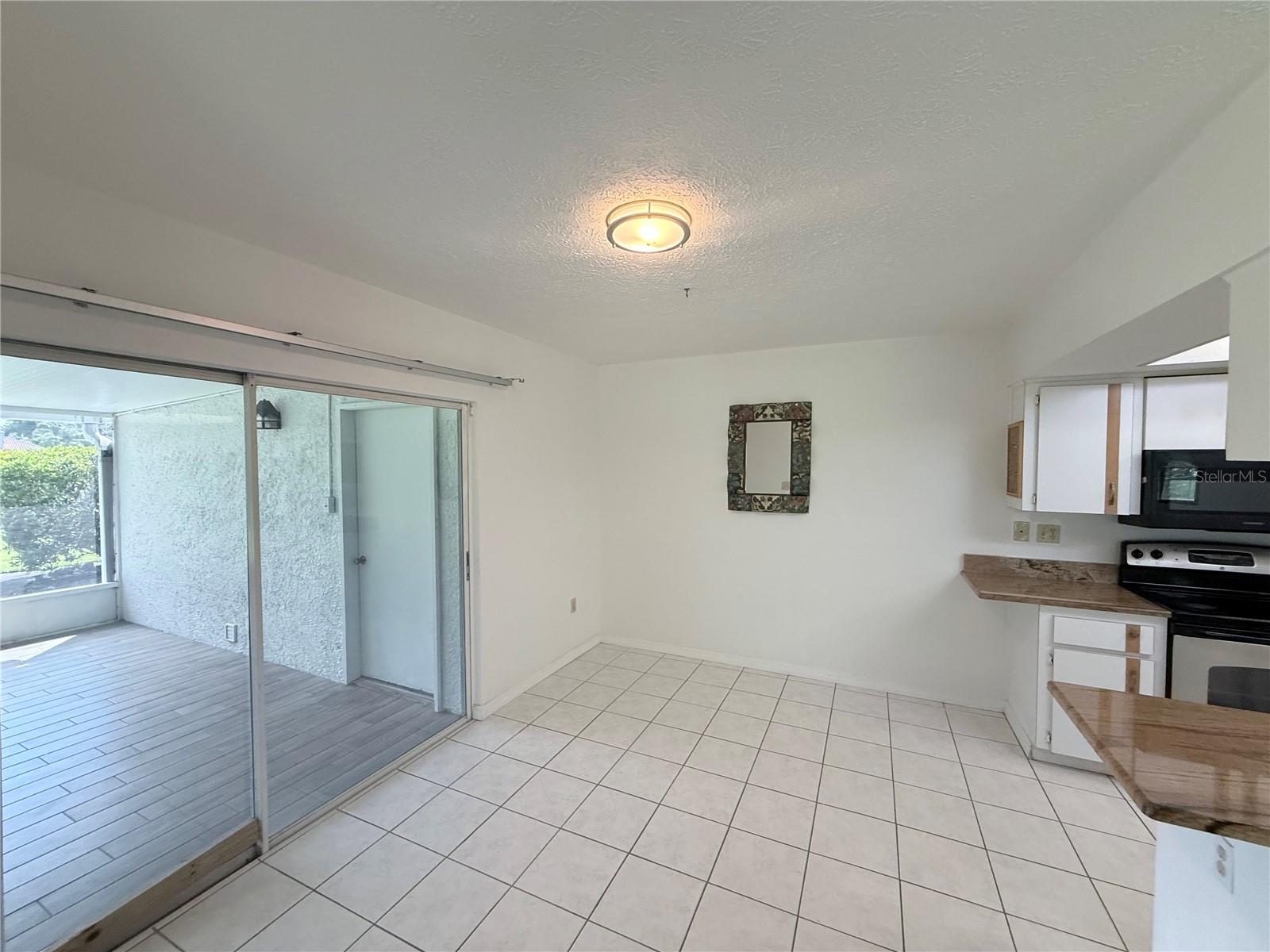 Empty tiled kitchen with a countertop and appliances beside sliding glass doors to a covered patio.