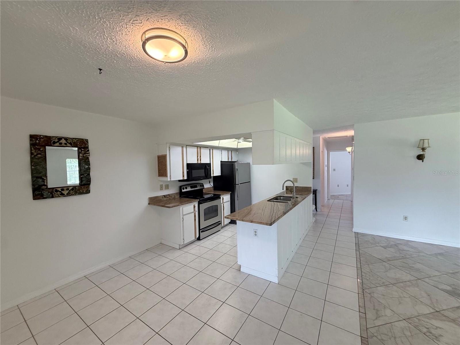 Kitchen with white cabinets, stainless appliances, a stone-look breakfast bar, and tiled flooring.