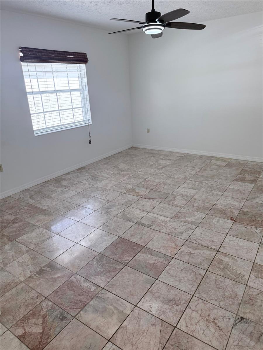 Empty room with mottled tile flooring, a window with blinds, and a ceiling fan.