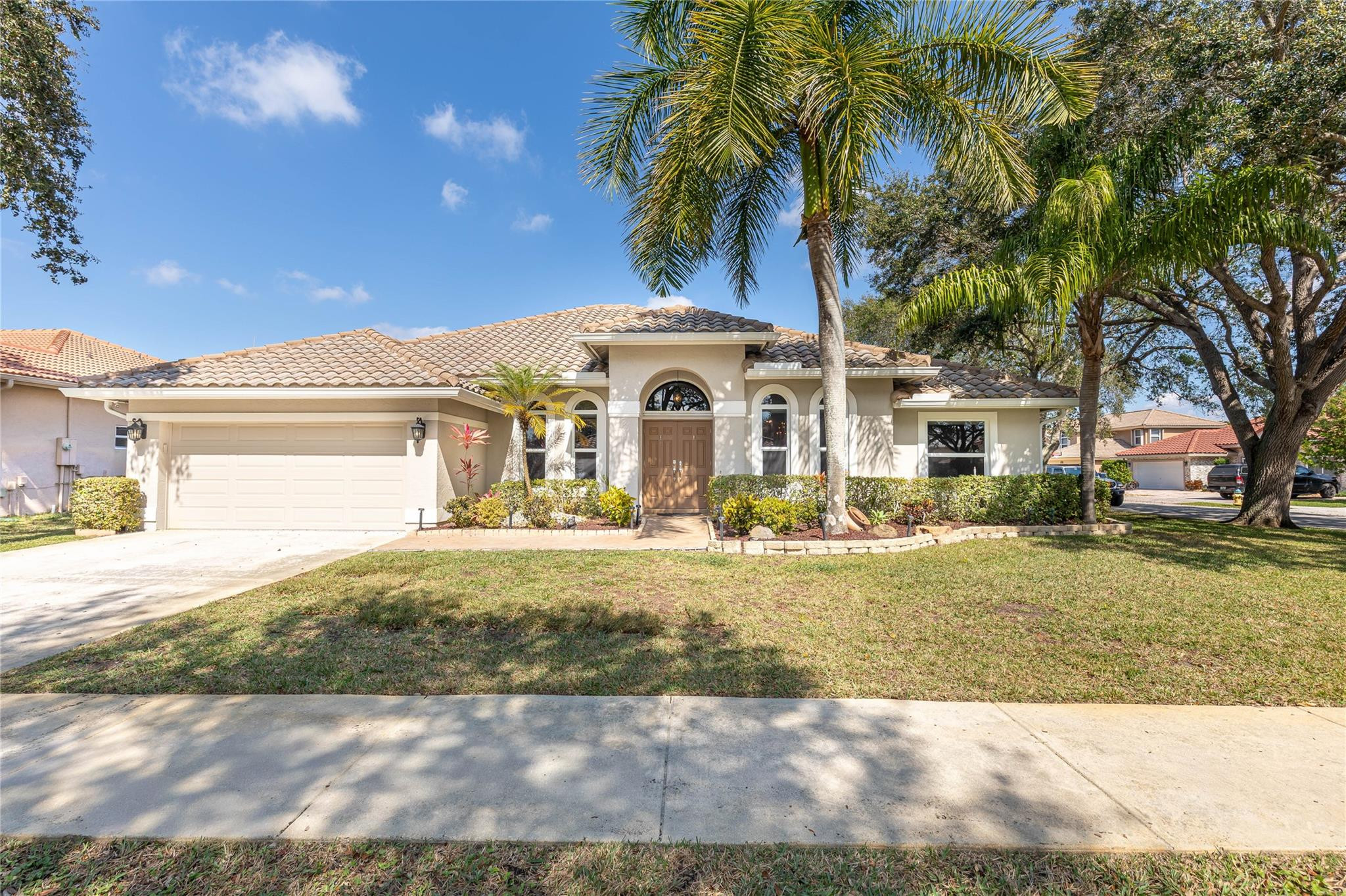 Single-story home with a tile roof, two-car garage, arched entry, and mature palm trees.