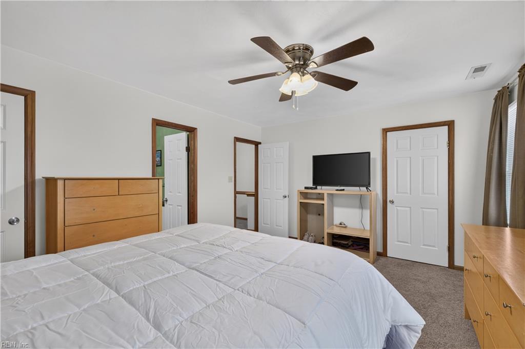 Bedroom with a white-covered bed, wooden dressers, television, and ceiling fan.