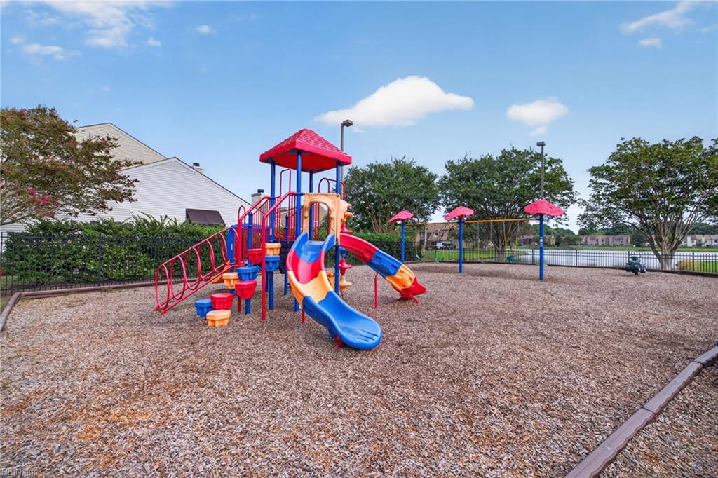 Community playground with colorful slides and climbing equipment beside a fenced pond.