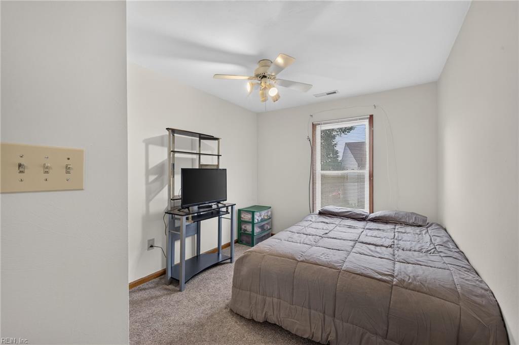 Bedroom with a gray quilted bed, window, ceiling fan, and television stand.