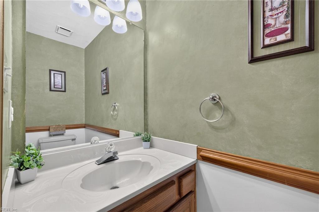 Bathroom vanity with a white oval sink, wood cabinetry, sage-green walls, and a large mirror.