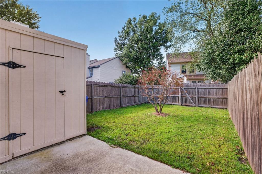 Fenced backyard with a green lawn, small tree, storage shed, and concrete patio.