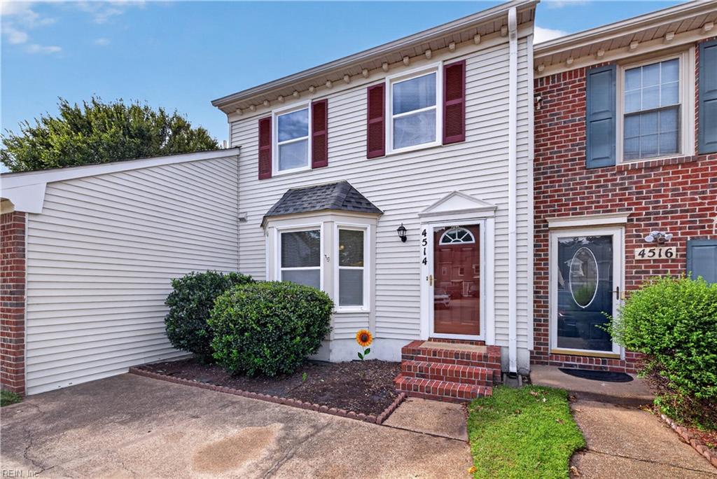 Attached townhouse with white siding, a red front door, brick steps, and a bay window.