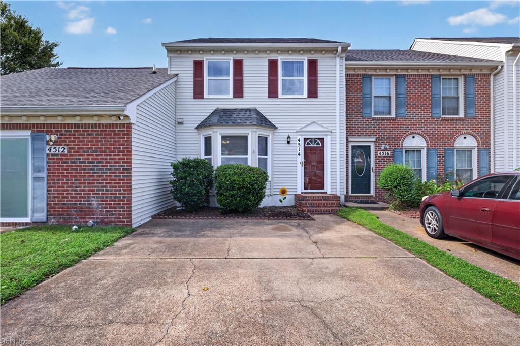 Front of a two-story attached home with white siding, red brick, red shutters, and a concrete driveway.