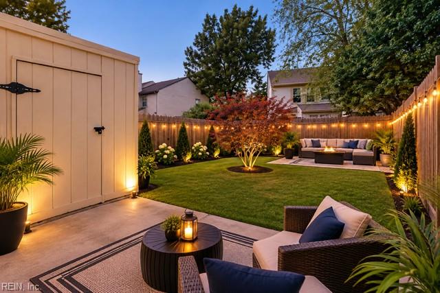 Backyard patio with wicker seating, a grassy lawn, illuminated privacy fence, and a shed.