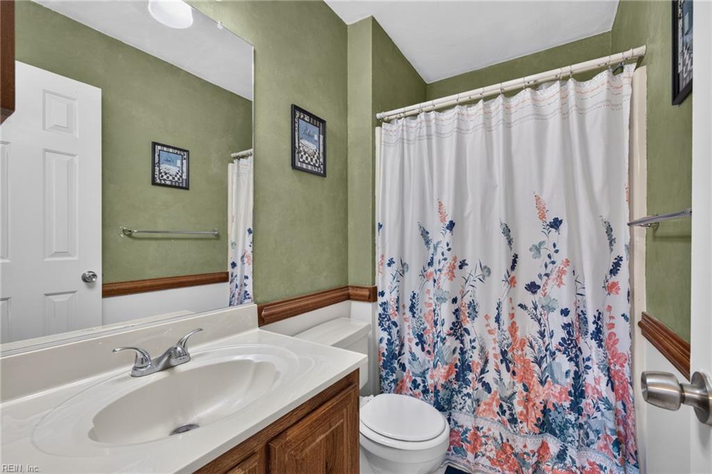 Bathroom with a white vanity, toilet, and floral shower curtain against olive-green walls.