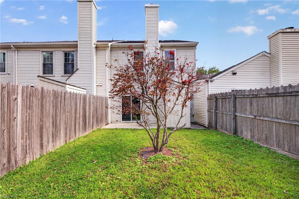 Fenced backyard with a green lawn, small red-leaf tree, and the rear of a two-story home.