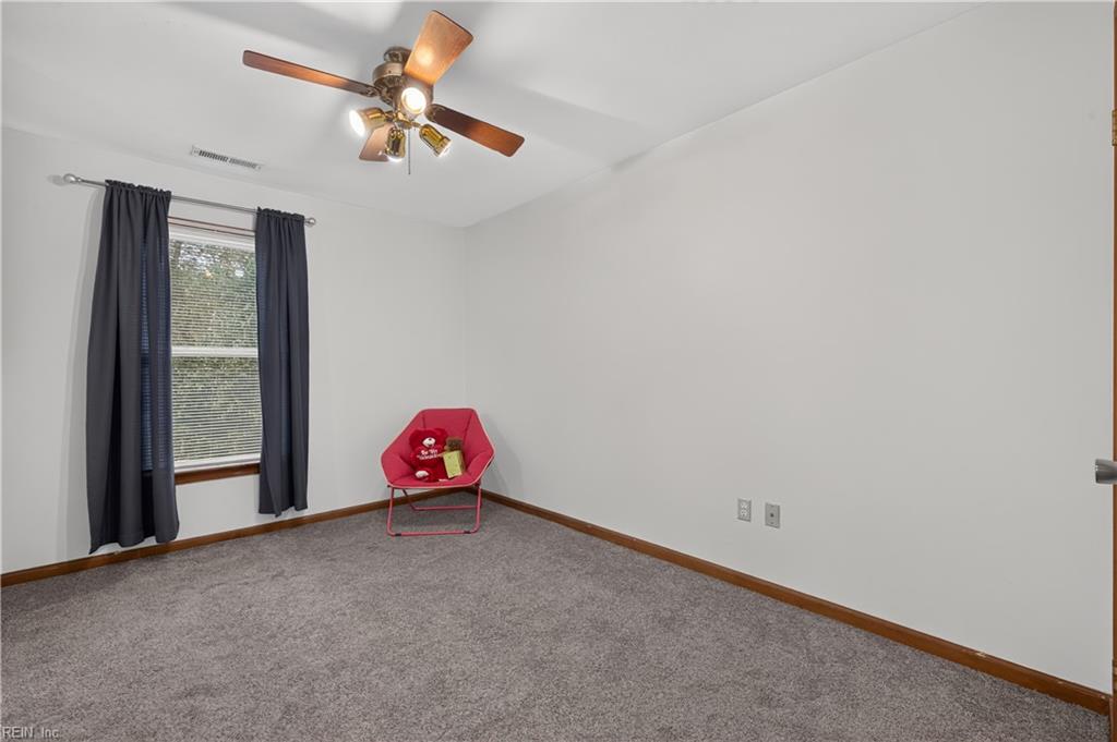 Bedroom with gray carpet, a curtained window, ceiling fan, and red chair in the corner.