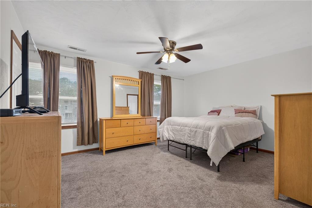 Furnished bedroom with a white bed, light wood dresser and mirror, and curtained windows.