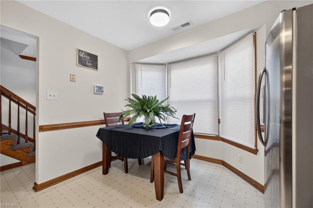 Dining area with a fern centerpiece, bay windows with blinds, and a stainless-steel refrigerator.