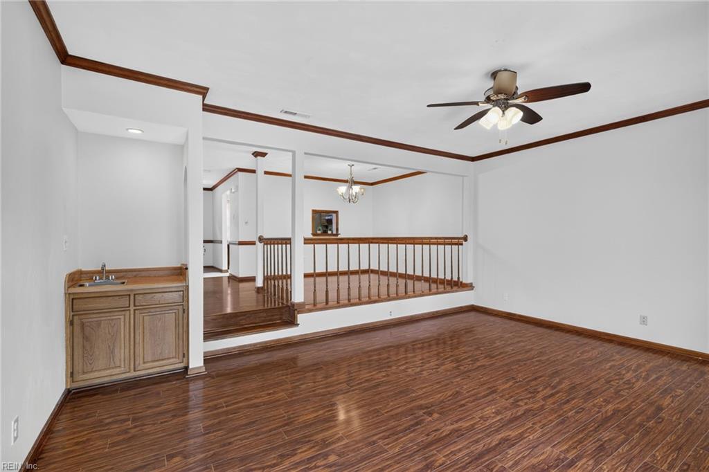Unfurnished room with glossy wood floors, a ceiling fan, and a raised landing behind a wooden railing.