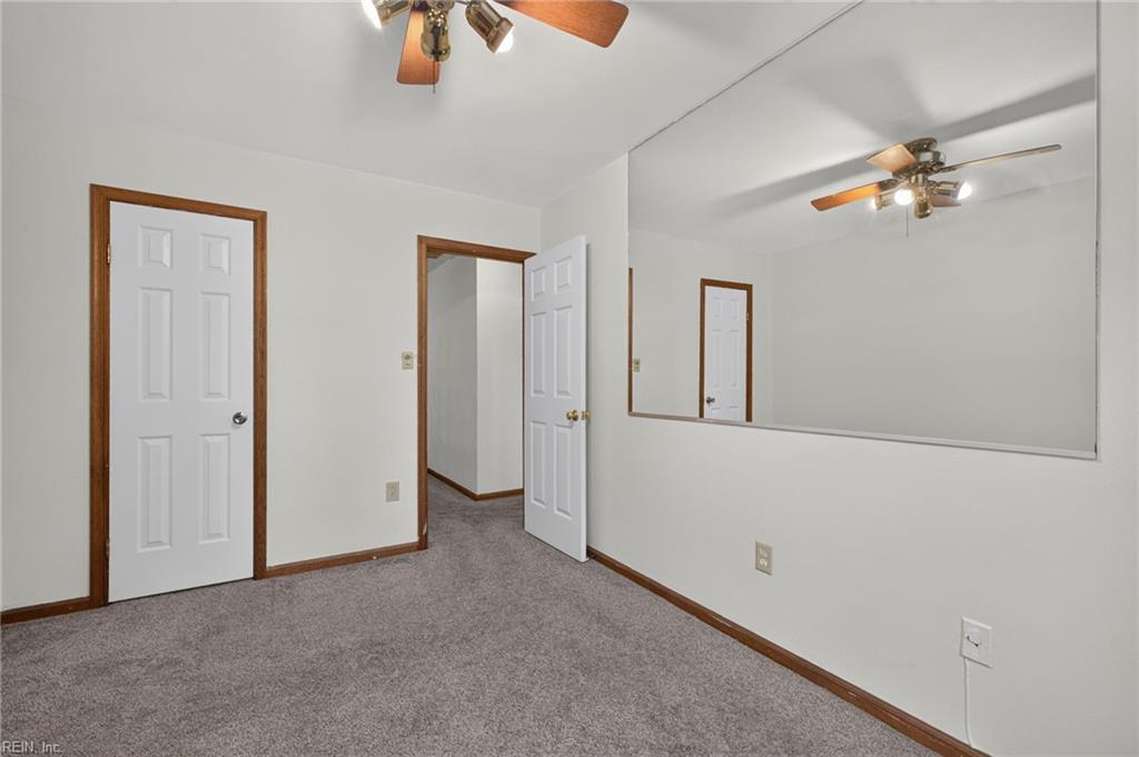 Empty bedroom with gray carpet, wood trim, a ceiling fan, and a large wall mirror.