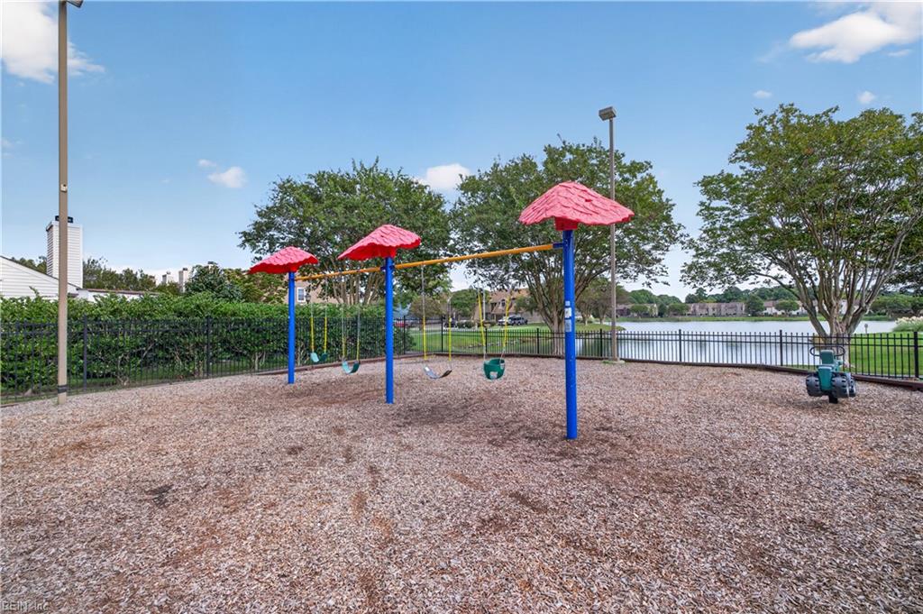 Fenced playground with red-roofed swings beside a pond.