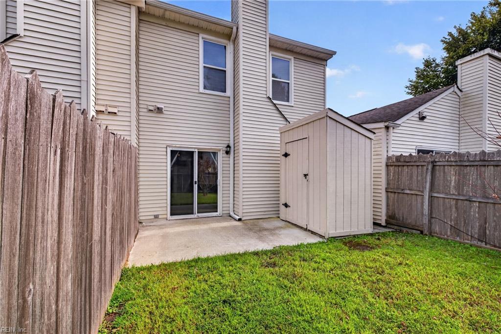 Fenced backyard with a storage shed, concrete patio, and lawn behind a beige two-story house.