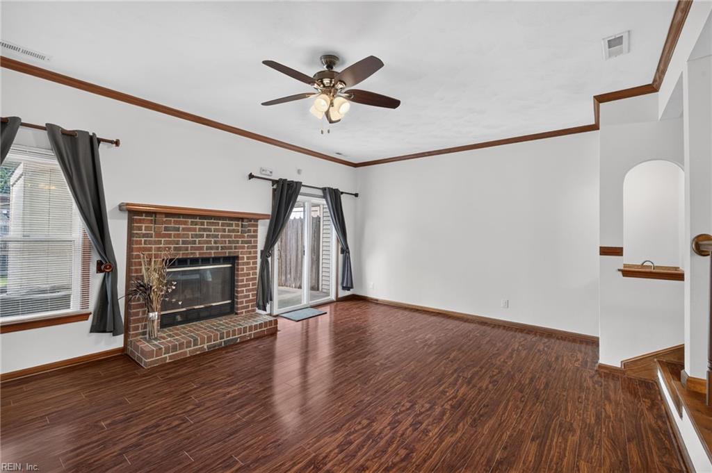 Empty living room with a brick fireplace, dark wood flooring, and sliding glass doors.