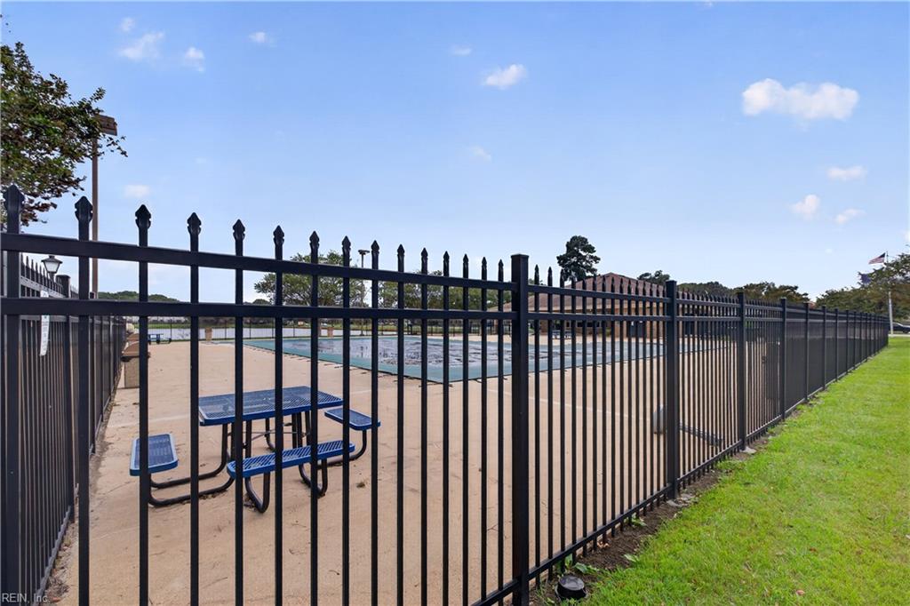 Outdoor swimming pool behind a black metal fence, with a blue picnic table on the deck.