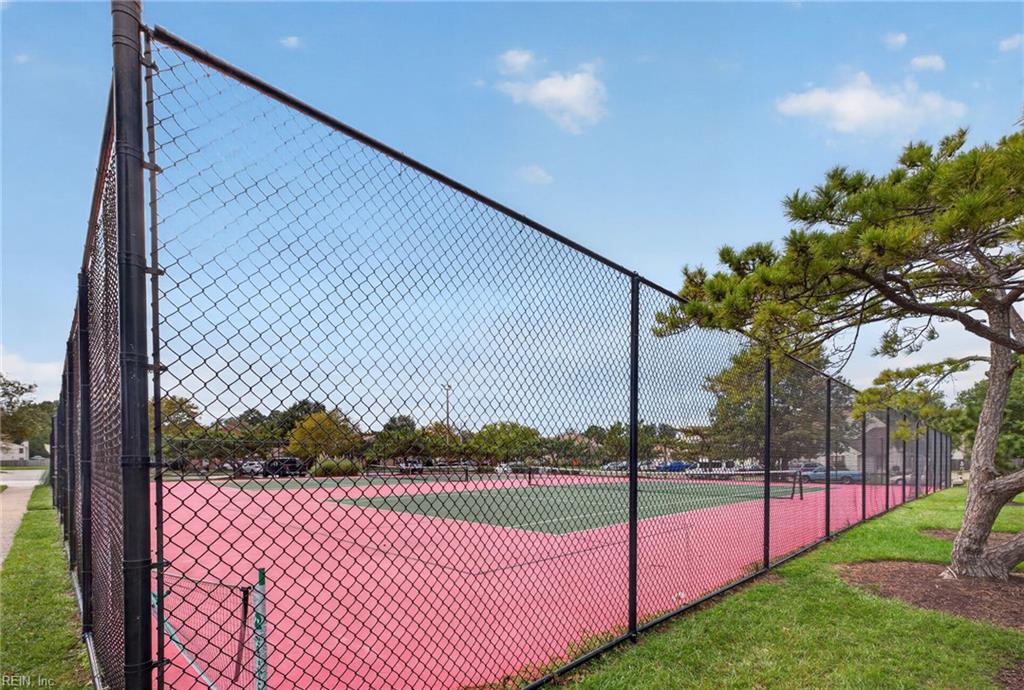 Fenced outdoor tennis court with pink and green playing surfaces and a pine tree beside it.