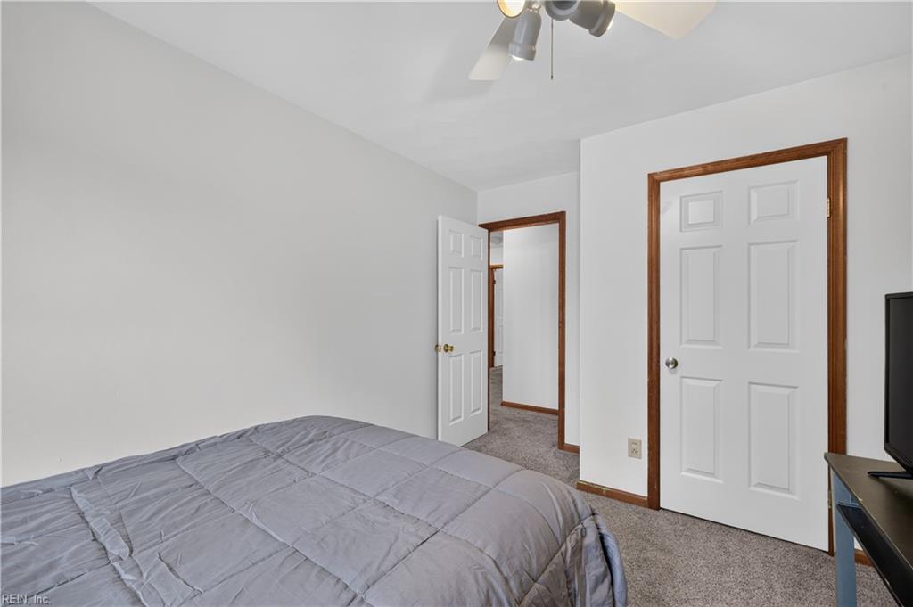 Bedroom with a gray quilted bed, carpeted floor, and wood-trimmed doors.