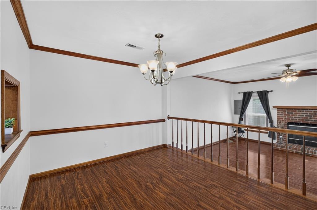 Hardwood-floored room with wood trim, a chandelier, and a railing beside a brick fireplace.