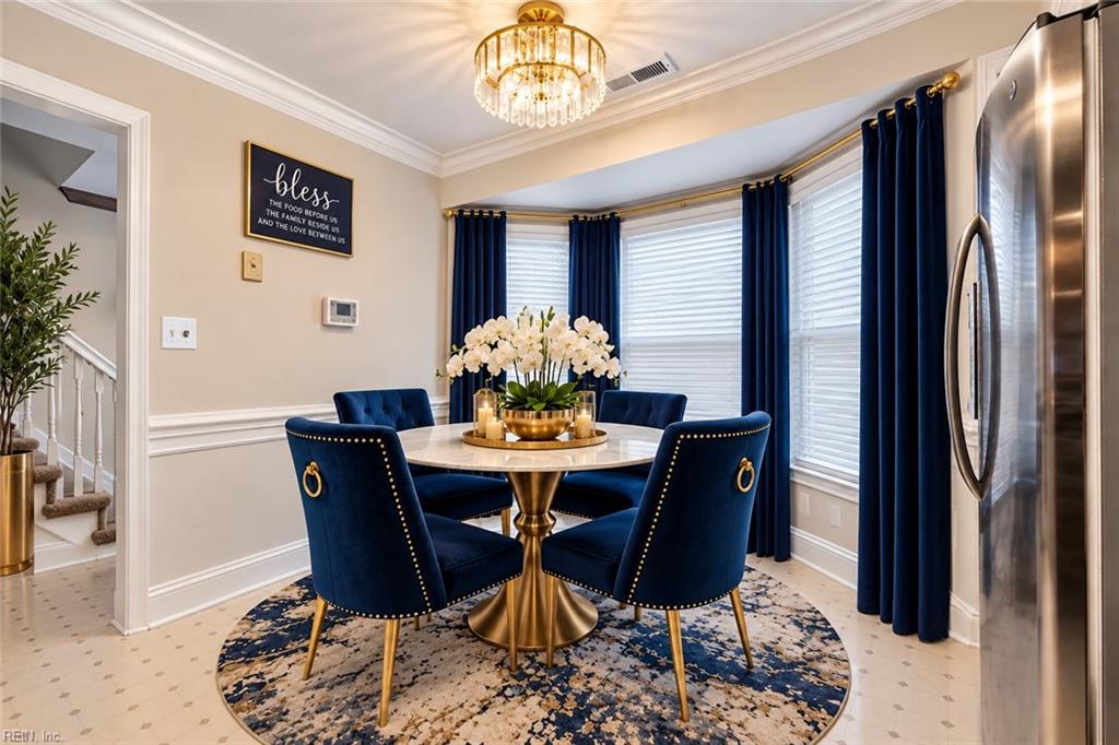 Dining room with navy chairs, a round gold table, and bay windows framed by dark curtains.