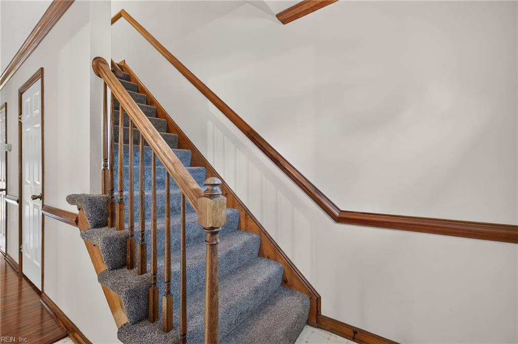Carpeted staircase with a polished wood railing and hardwood flooring in the adjacent hall.