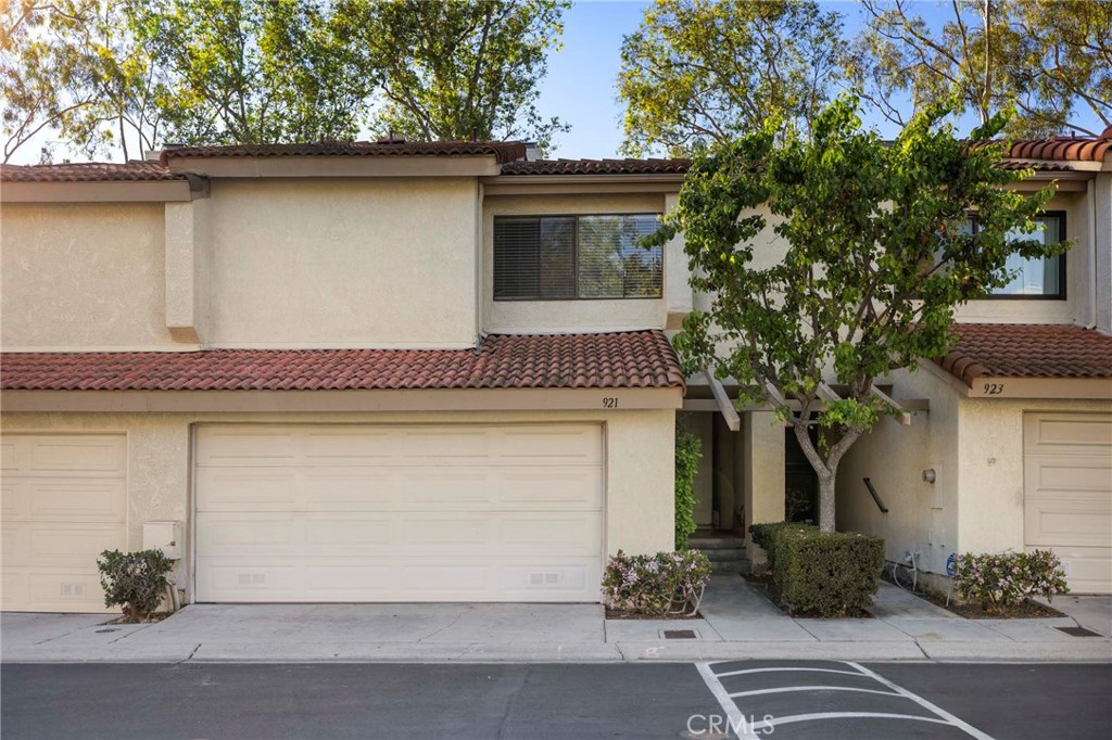 Attached two-story home with a tiled roof, large garage, and mature tree in front.