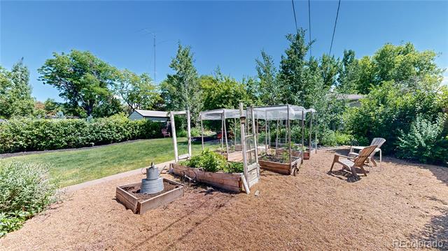 Backyard garden with raised beds beneath a trellis and two Adirondack chairs.
