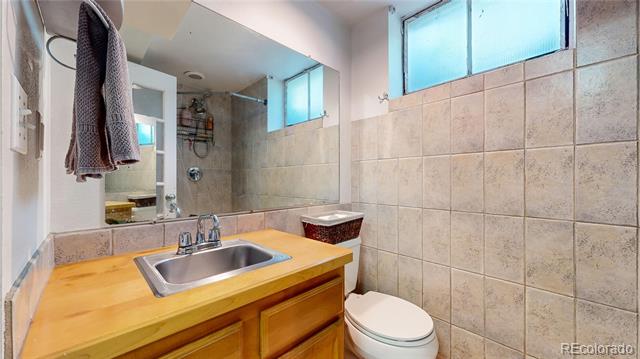 Bathroom with a wood vanity, tiled walls, toilet, and high frosted windows.