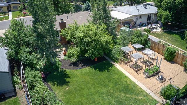 Aerial view of a backyard with a broad lawn, mature trees, and raised garden beds.