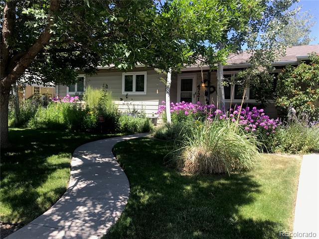 Single-story home with a curved walkway, purple flowers, and mature shade trees.
