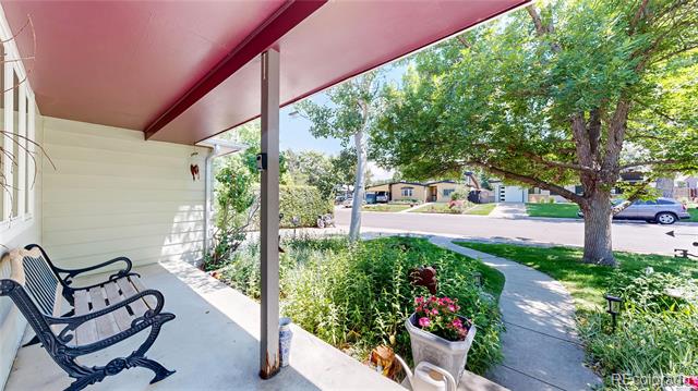 Covered front porch with black rocking chairs overlooking a flower garden and tree-lined street.