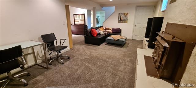 Furnished basement living area with a black sectional, ottoman, office chairs, and television.