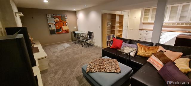 Furnished basement living area with a black leather sectional, ottoman, desk, and built-in shelving.