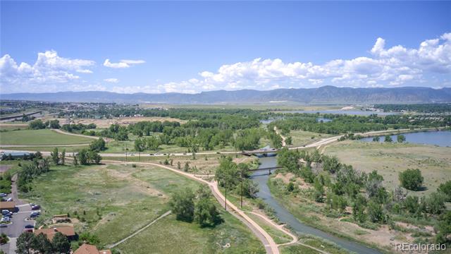 Aerial view of a creek winding through green open space, with paths and mountains in the distance.