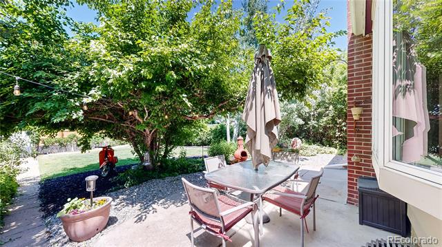 Backyard patio with a glass-top dining table beneath a large leafy shade tree.