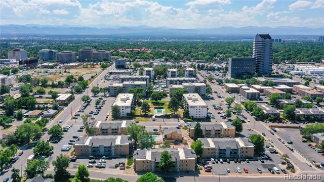 Aerial view of Denver buildings and tree-lined streets, with a prominent office tower and distant mountains.