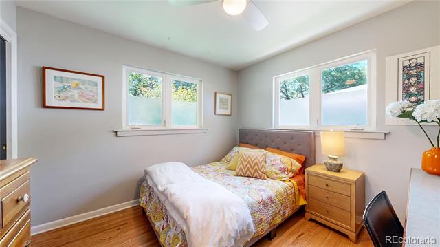Bedroom with a colorful patterned bed, hardwood floors, and windows on two walls.