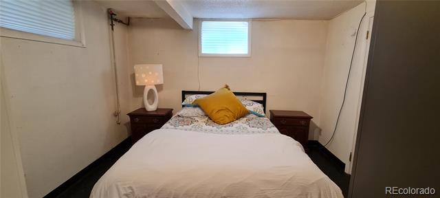 Bedroom with white bedding, a mustard-yellow pillow, dark nightstands, and small high windows.