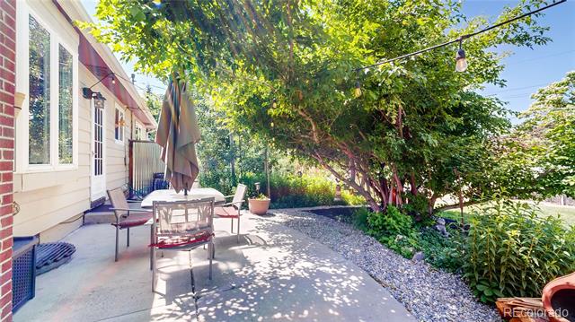 Back patio with an outdoor dining set, closed umbrella, string lights, and mature shade trees.
