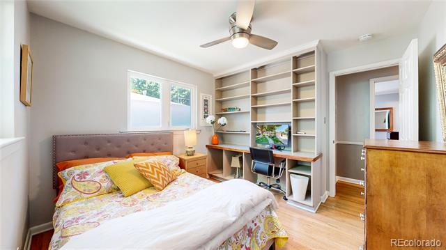 Bedroom with a colorful bed, built-in desk and shelving, and ceiling fan.