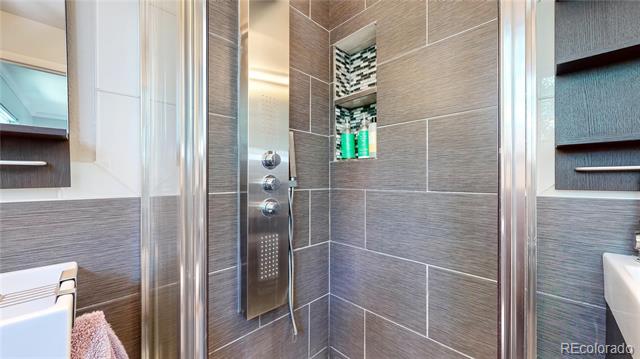 Gray-tiled shower with chrome controls, recessed shelf, and glass doors.