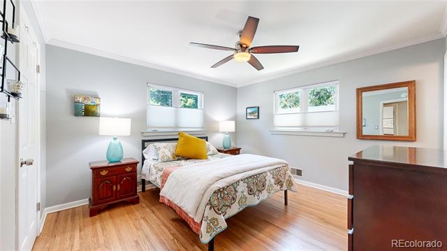 Bedroom with hardwood floors, two windows, and a bed with a floral skirt and yellow accent pillow.