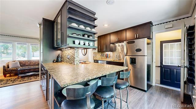 Kitchen with a large stone island, dark cabinetry, stainless steel appliances, and an adjoining sitting area.