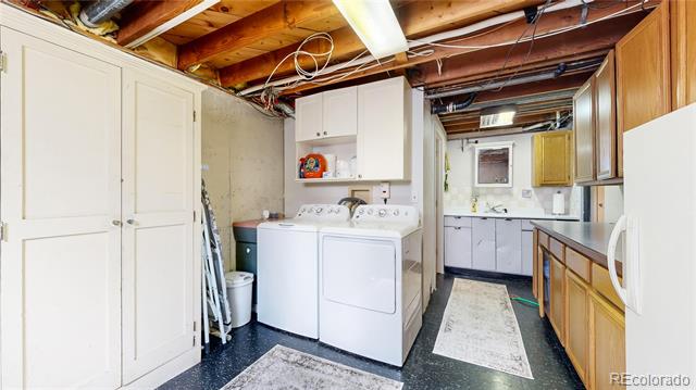 Basement laundry room with a washer and dryer, white cabinets, and exposed ceiling joists.